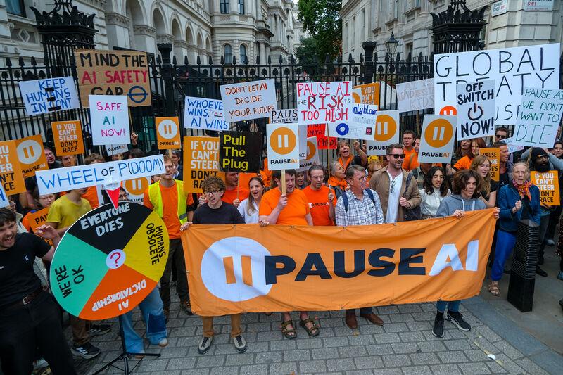 Protesters holding a PauseAI banner, placards and a Wheel of P(doom) in front of the gates of Downing Street