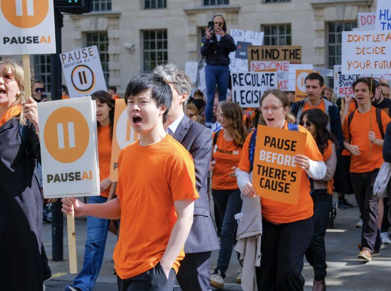 Volunteers in orange T-shirts chanting and carrying PauseAI signs